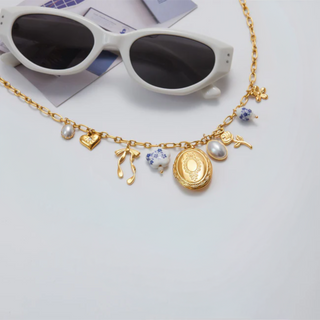 Gold necklace with charms on a white surface next to sunglasses